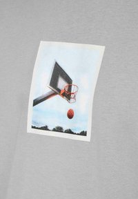 T-shirt di cotone grigia con una grafica rettangolare di un canestro da basket con un pallone da basket in volo contro un cielo azzurro.