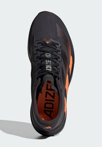Fekete sportcipő narancssárga részletekkel, hálós felsőrésszel és texturált mintázattal. Párnázott szegéllyel és fűzőkkel rendelkezik. Márkajelzés a nyelven és a talpbetéten.