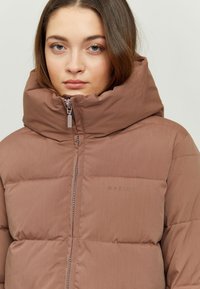 Puffy brown jacket with a high collar, featuring quilted sections and a zip closure. Logo "MAZINE" in subtle lettering on the front.