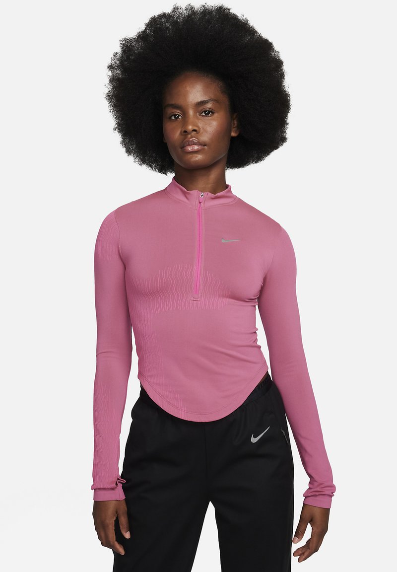 Top atlético de manga larga rosa con cuello con media cremallera, patrones texturizados en el pecho y logo de Nike. Parte inferior negra con marca de Nike.