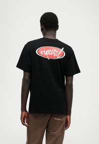 Schwarzes Baumwoll-T-Shirt mit einem auffälligen roten ovalen Logo und weißem Text auf dem Rücken. Einfaches Design mit kurzen Ärmeln und rundem Halsausschnitt.