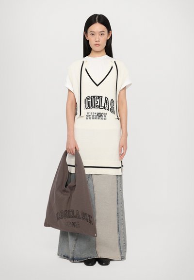 Tunique en tricot blanche avec des lettres et des rayures noires, superposée sur une jupe en denim. Sac fourre-tout en tissu gris affiché. Design élégant et minimal.