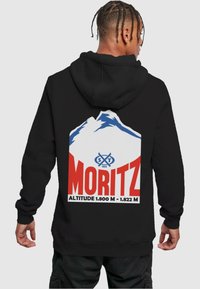 Fekete kapucnis pulóver, amelynek hátulján egy nagy grafikai tervezés található, kék és fehér hegyekkel, valamint élénk piros szöveggel, amely "MORITZ" feliratot és magassági adatokat tartalmaz.