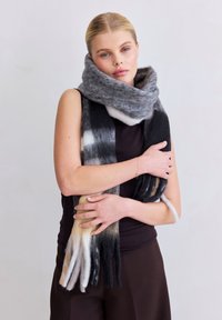 Écharpe tricotée douce à plusieurs tons, en gris, noir et crème, arborant un design long avec des franges et un aspect texturé et confortable.