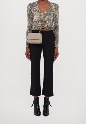 Top med ormtryck och långa ärmar, tillsammans med svarta, åtsittande byxor och eleganta svarta ankelboots. Cremefärgad vadderad handväska med detaljer i guld.