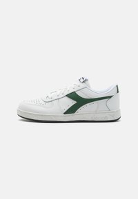 White leather sneaker with green accents, perforated detailing on the toe, flat laces, and a rubber sole. Features a textured side logo.