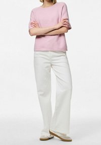 Světle růžový pletený svetr s krátkými rukávy, kombinovaný s bílými kalhotami širokého střihu a béžovými botami. Svetr má kulatý výstřih a měkkou strukturu.