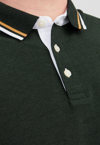 Polo shirt verde scuro con colletto bianco a strisce arancioni e bianche, patta con tre bottoni e tessuto testurizzato.