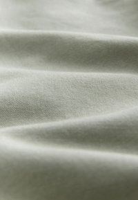 Tessuto verde chiaro con trama tessuta, che mostra pieghe morbide e una superficie liscia e leggermente lucida.