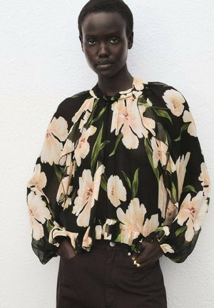 Blusa nera con grande motivo floreale crema, scollatura arricciata, maniche a sbuffo e orlo volant, abbinata a pantaloni marroni scuri.