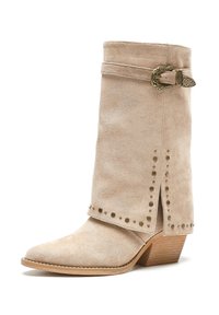 Botín de ante beige hasta el tobillo con punta afilada, tacón apilado, hebilla metálica decorativa y acentos con tachuelas en la costura lateral.