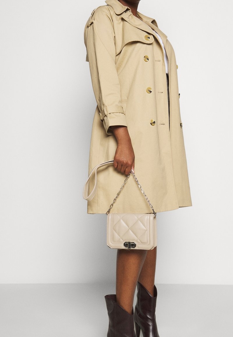 Beige trenchcoat med guldfärgade knappar, kombinerad med en quiltad beige handväska med silverkedja och mörkbruna knähöga stövlar.