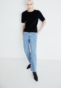 Black knitted short-sleeve top, light blue straight-leg jeans, and black pointed-toe ankle boots against a plain white background.