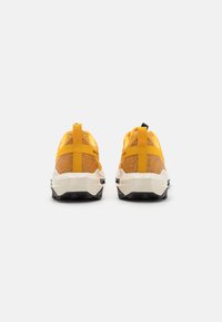 Baskets de sport jaunes avec une tige texturée, des accents noirs et une semelle robuste. Comprend des languettes de traction et des éléments de design géométrique.