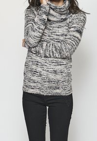 Pull à col bénitier en tissu doux et texturé avec un motif rayé noir et blanc. Assorti à un pantalon en denim noir, avec de légères ornements discrètes.