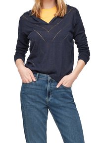 Marinblå hoodie med V-ringning, prydd med diagonala gyllene linjer, långa ärmar och en avslappnad passform, matchad med ljusblå jeans.