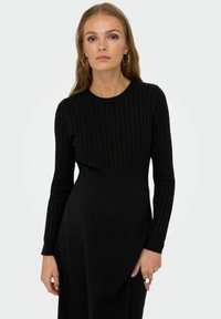 Robe en tricot côtelé noire à manches longues, dotée d'un corsage ajusté et d'une jupe fluide. Tissu texturé avec une finition lisse.
