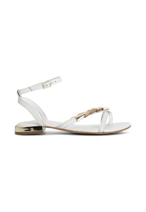 Hvid flad sandal med tynde stropper, guldkædedetalje på frontstroppen, ankelspænde og metallisk gyldent lavt hæl accenter.