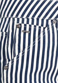 Blå och vit randig tyg, denimmaterial, med en framficka med silverfästen och en logotag.