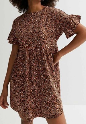 Femme portant une robe marron à manches courtes avec imprimé léopard, des détails à volants et une main posée sur la hanche.