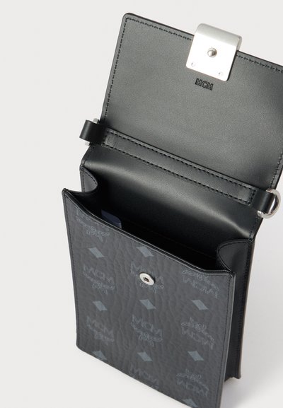 Μαύρο δερμάτινο πορτοφόλι με ασημένια πόρπη, με εσωτερικό σε γκρι αποχρώσεις με υφή και επαναλαμβανόμενο μοτίβο λογότυπου MCM. Περιλαμβάνει θήκες για κάρτες και διαμερίσματα.