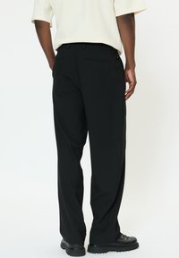 Fekete nadrág egyenes szárú kialakítással, két hátsó zsebbel és texturált anyagból. Fekete fűzős csizmával párosítva.