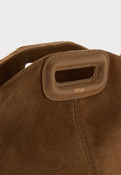 Sac en daim marron avec une découpe rectangulaire en cuir pour la poignée et un petit logo doré "maje" sous la poignée.