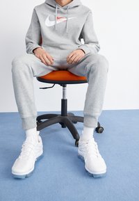 Szary hoodie i dresy Nike, białe trampki z przezroczystą podeszwą, siedzący na pomarańczowym krześle na jasnym tle.