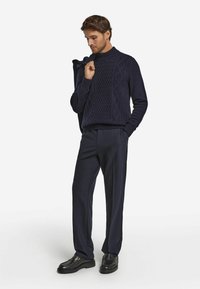 Marineblauer gestrickter Pullover mit einem strukturierten Rautenmuster, kombiniert mit dunkelgrauen, maßgeschneiderten Hosen und schwarzen Schuhen. Warmer Stoff, schlanke Passform.