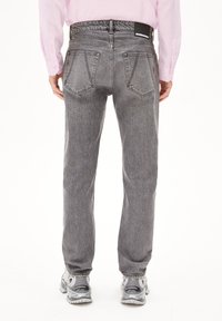 Graue Denim-Jeans mit geradem Schnitt, fünf Taschen und einem schwarzen Markenlabel am Bund, kombiniert mit hellgrauen Sneakers.