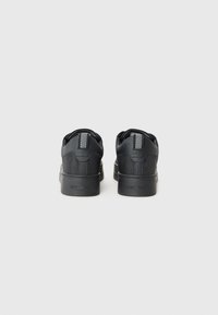 Schwarze Sneaker mit einem oberen aus strukturiertem Stoff, Gummisohle und Ferse mit Fischgrätenmuster. Minimalistisches Design mit sauberer Verarbeitung.