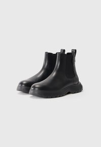 Bottines Chelsea noires en cuir lisse, avec des panneaux élastiques sur les côtés, des languettes de tirage et des semelles en caoutchouc texturé. Design à bout rond.