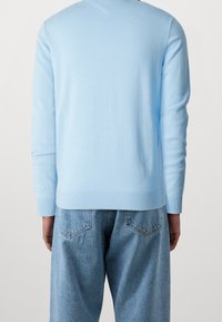 Hellblauer Strickpullover mit Rundhalsausschnitt, gerippten Bündchen und Saum, getragen zu hoch taillierten, ausgewaschenen blauen Jeans. Glatte Textur.