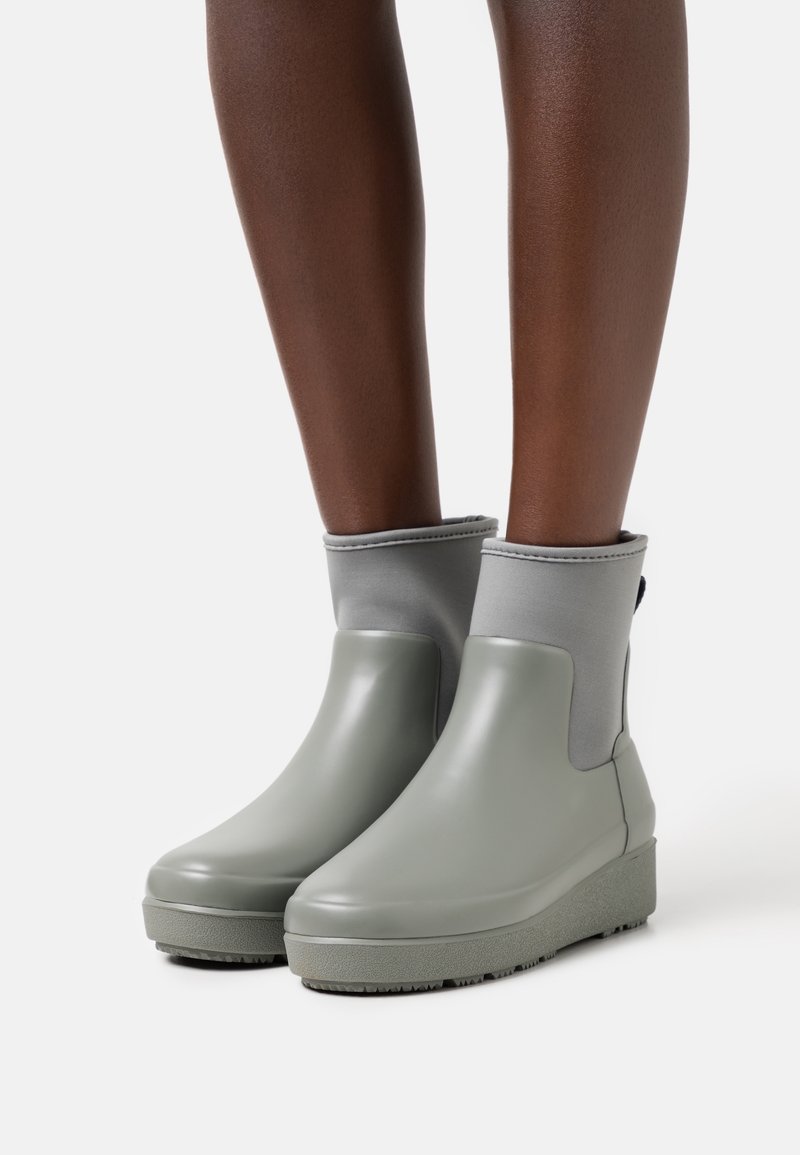 Zielone wodoodporne botki z gładkim wykończeniem, szarym elastycznym kołnierzem, podeszwą na koturnie oraz teksturowaną gumową podeszwą zapewniającą przyczepność.