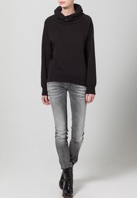 Felpa nera con collo a scialle, maniche raglan e vestibilità ampia. Abbinata a jeans skinny grigi e stivaletti neri con lacci.