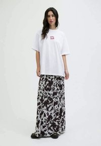 Balta per didelė t-shirt su raudonu tekstu "STAY WILD", derinama su ilga juoda ir balta marginta sijonu, dėvima su juodais batais.