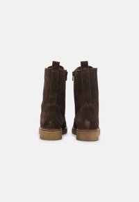 Stivali alla caviglia in suede marrone con una superficie liscia, cerniere laterali e linguette, dotati di una suola in gomma di un marrone chiaro a contrasto.
