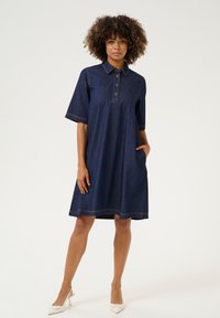 Denim jurk met een kraag, korte mouwen en zijzakken. Heeft contrasterende stiksel en een losse A-lijn vorm.