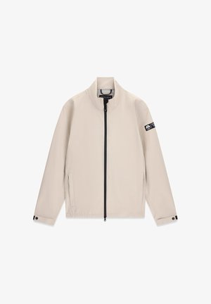 Veste légère beige avec fermeture éclair avant noire, deux poches latérales, col montant, poignets réglables et écusson logo sur la manche gauche.