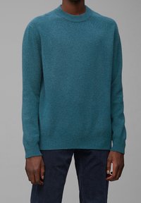 Tealová vlna svetru s kulatým výstřihem, dlouhými rukávy a žebrovanými manžetami. Měkká textura, volný střih a minimalistický design.