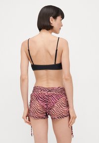 Juodas bikini viršus su reguliuojamomis petnešėlėmis, derinamas su rožiniais ir juodais dryžuotais šortais, pasižyminčiais tekstūruotu paviršiumi ir šoninėmis raištelėmis.