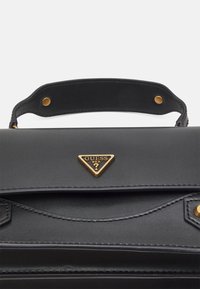 Mustang black leather handbag with gold hardware, showcasing a triangular logo, a sturdy top handle, and detailed stitching on the flap.