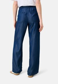 Brettbenade denimbyxor i mörkblått med elastisk midja, bakfickor och en slät textur. Skorna har en ljusfärgad remdesign.