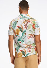 Camisa tropical de manga corta en blanco, con un vibrante estampado floral en verdes, amarillos y rojos. Tejido ligero, ajuste relajado.