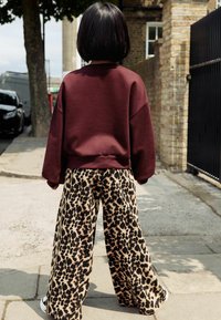 Bordeauxfarbene, übergroße Sweatshirt kombiniert mit lockeren, weiten Hosen im Leopardenmuster. Texturiertes Material, lebendiger Farbkonstrast und markante Muster.