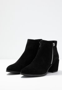 Botines de ante negros con punta afilada, cremalleras laterales y tacón ancho, con una textura suave y acentos mínimos.