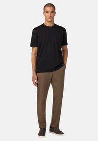 Juodas trumpomis rankovėmis marškinėliai iš minkštos medžiagos, derinami su rudos spalvos siaurais kelnais ir tamsiais sportbačiais. Paprastas dizainas su minimaliu akcentu.