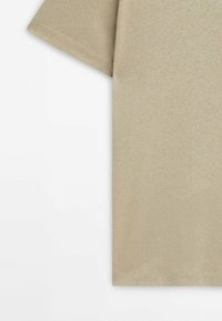 T-shirt beige en coton à manches courtes avec coutures visibles près de la manche et de l’ourlet inférieur sur fond blanc.