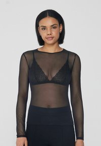 Schwarzes Langarmshirt aus transparentem Material, mit rundem Halsausschnitt und leicht tailliertem Schnitt, über einem Spitzen-Bralette getragen.