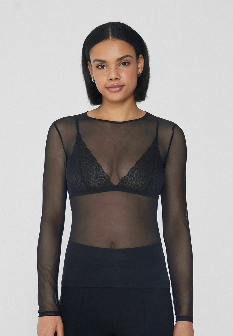 Schwarzes Langarmshirt aus transparentem Material, mit rundem Halsausschnitt und leicht tailliertem Schnitt, über einem Spitzen-Bralette getragen.
